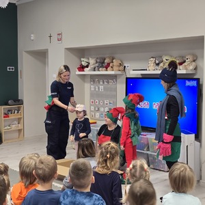 zdjęcie przedstawia policjantkę pokazującą dzieciom jak prawidłowo ubierać się zimą