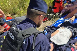 Policjanci i strażacy udzielają pomocy osobie poszkodowanej podczas ćwiczeń służb ratunkowych w terenie.
