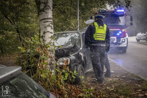 zdjęcie przedstawia wrak z unoszącym się dymem spod maski i policjantów udzielających pomocy