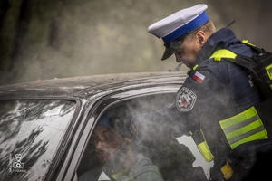 zdjęcie przedstawia wrak z unoszącym się dymem spod maski i policjantów udzielających pomocy