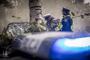 zdjęcie przedstawia wrak z unoszącym się dymem spod maski i policjantów