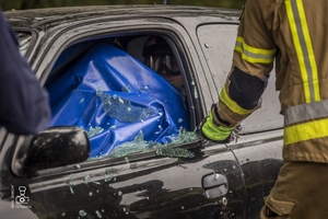 zdjęcie przedstawia wrak samochodu i strażaka rozbijającego szybę
