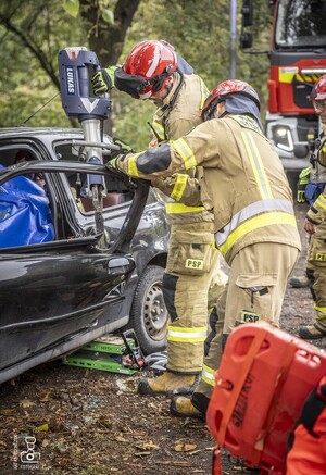 zdjęcie przedstawia wrak samochodu i strażaków rozcinających drzwi