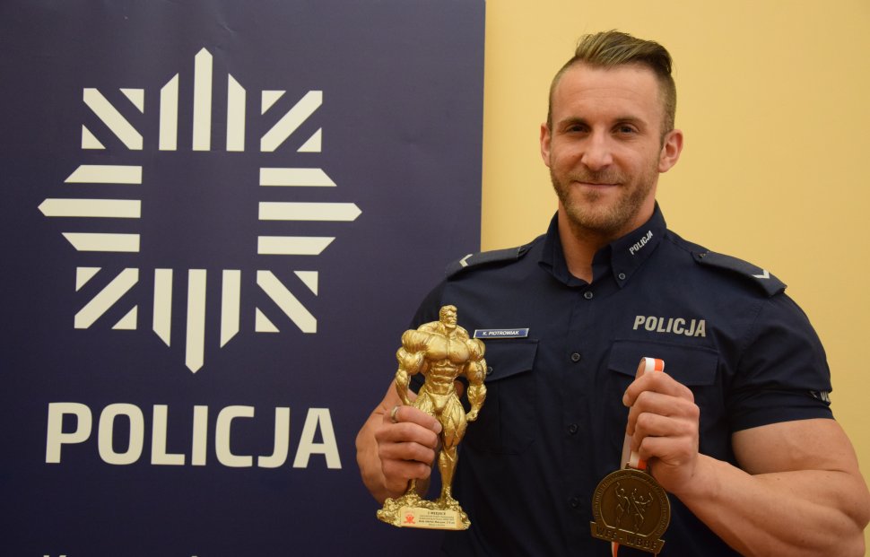 Na zdjęciu widać sierżanta Kamila Piotrowiaka, który trzyma w ręku złoty medal i statuetkę strongmena