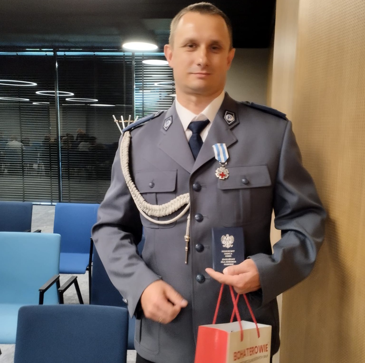 na zdjęciu dzielnicowy Modrzyński z legitymacją honorowego krwiodawcy w ręce oraz medalem na mundurze