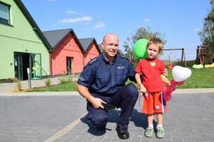 Na fotografii widać kucającego policjanta, przy którym stoi mały chłopiec.