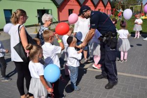Na fotografii wdać policjanta, który rozdaje grupie dzieci odblaskowe opaski.