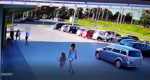 zdjęcie przedstawia ujecie z kamery monitoringu na którym klienci sklepu wchodzą do sklepu  a na parkingu mężczyzna dokonuje rozboju