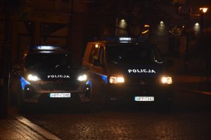 Na zdjęciu widać zaparkowane obok siebie dwa policyjne radiowozy. Zdjęcie wykonane w nocy.