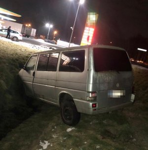 Na zdjęciu widać Volkswagena Transportera, który wpadł do przydrożnego rowu. W tle zdjęcia widać stację paliw oraz policjanta przy radiowozie.