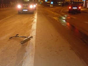 Na zdjęciu widać leżącą na drodze hulajnogę.  W tle zdjęcia widać policyjne radiowozy oraz uszkodzony samochód osobowy.