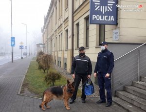 Na zdjęciu widać sierżanta sztabowego Roberta Judę, który stoi obok seniora i jego psa przed budynkiem Komendy Powiatowej Policji w Tarnowskich Górach