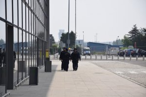 Na zdjęciu widać grupę policjantów przemieszczających się w kolumnie, wzdłuż terminalu lotniczego.