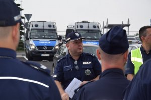 Na zdjęciu widać Komendanta Powiatowego Policji w Tarnowskich Górach młodszego inspektora Sławomira Bylickiego podczas odprawy służbowej. Za Komendantem widać policyjne radiowozy.