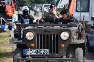Na zdjęciu widać samochód wojskowy, za którym jedzie policjant na motocyklu