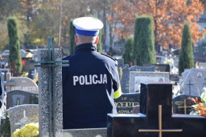 Policjant z drogówki stoi na cmentarzu przy grobach