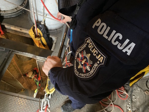 na zdjęciu policyjna naszywka na lewym ramieniu policjanta, w podłodze otwarty właz do górniczego szybu
