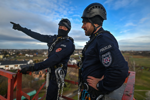 na zdjęciu policjanci stojący na wieży szybowej kopalni, jeden z nich wskazuje na coś palcem, drugi podpiera się o swoje biodra