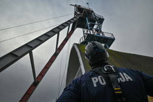 na zdjęciu policjant u podnóży wieży szybowej kopalni, który spogląda w górę