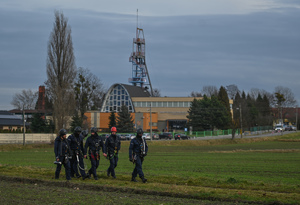 na zdjęciu policjanci maszerujący polem, za nimi w oddali widać wieżę szybową kopalni