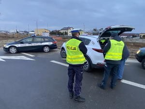 na zdjęciu policjant i funkcjonariusz służby celno-skarbowej w trakcie kontroli białego pojazdu na drodze