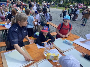 na zdjęciu policjantka z dziećmi przy stola, na którymi leżą kartki i przybory do malowania