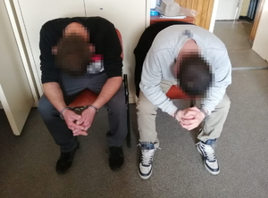 na zdjęciu zatrzymani siedzą na krześle ze spuszczonymi głowami, ręce mają zakute w kajdanki