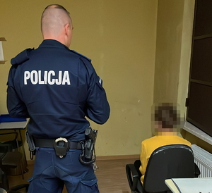 na zdjęciu policjant przy zatrzymanym, który siedzi tyłem na krześle