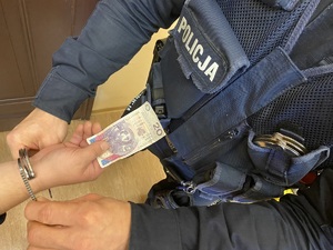 na zdjęciu ręka osoby, która wręcza policjantowi banknot 20 złotych, która w tym momencie zakuwa w kajdanki mundurowy