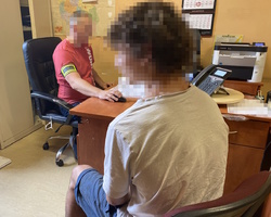na zdjęciu zatrzymany siedzący przy biurku, za biurkiem policjant