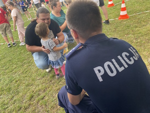 na zdjęciu policjant a przed nim dziecko z rodzicami