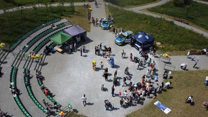 zdjęciu z lotu ptaka z widokiem na teren imprezy, gdzie widoczni są uczestnicy, policyjne radiowozy oraz namiot