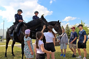 na zdjęciu policjanci na koniach a przed nim dzieci