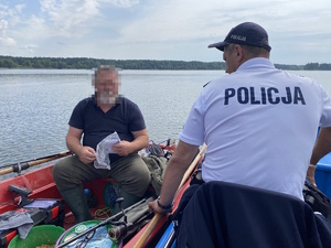 na zdjęciu policjant w trakcie rozmowy z wędkarzem na łódce, który z folii wyciąga dokumenty