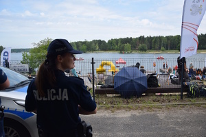 na zdjęciu policjantka przed radiowozem, która patrzy w prawo, przed nią teren zawodów