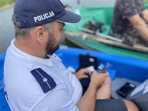 na zdjęciu policjant z alkomatem przy jednej z łódek nad zalewem