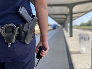 na zdjęciu ręka policjanta, w której trzyma radiotelefon, widoczny także pas główny umundurowania, na którym widoczna broń i kajdanki
