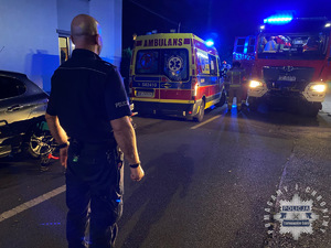 na zdjęciu policjant stojący na jezdni przed karetką pogotowia i wozem strażackim