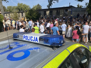 na zdjęciu dach radiowozu, a przed nim policjant i publiczność przy jezdni na trasie pochodu