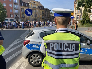 na zdjęciu policjant, przed nim radiowóz, a przed radiowozem publiczność oglądająca pochód