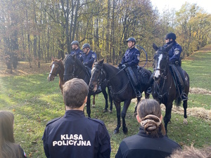 na zdjęciu policyjni jeźdźcy na koniach przed młodzieżą w mundurach z napisem klasa policyjna