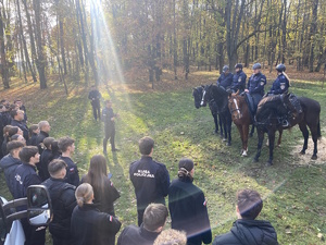 na zdjęciu policjanci na konia przed młodzieżą stojąca na trawie w dwuszeregu