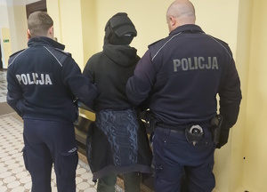 na zdjęciu policjanci z zatrzymanym mężczyzną w korytarzu