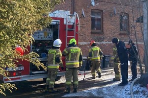 na zdjęciu policjanci i strażacy przy wozie strażackim i budynku