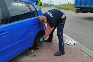 na zdjęciu policjant w trakcie wymiany koła w pojeździe