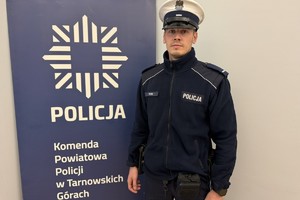 na zdjęciu policjant przy banerze z napisem policja komenda powiatowa policji w tarnowskich górach
