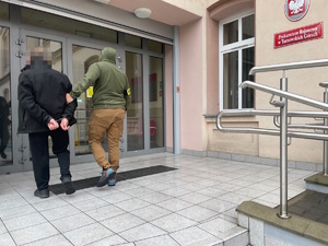 na zdjęciu policjant po cywilu z zatrzymanym przed budynkiem prokuratury