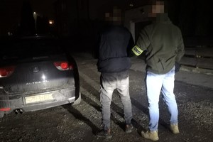 na zdjęciu policjant po cywilu z zatrzymanym przy samochodzie, na którym jest tekturowa tablica rejestracyjna