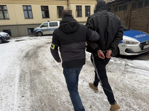 na zdjęciu policjant po cywilu prowadzi zatrzymanego na podwórku