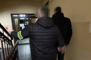 na zdjęciu policjant po cywilu, prowadzi zatrzymanego korytarzem